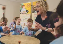 A happy Monkey Music teacher playing a large drum joined by some happy toddlers