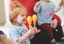 Happy toddler at Monkey Music class shaking colourful maracas while smiling
